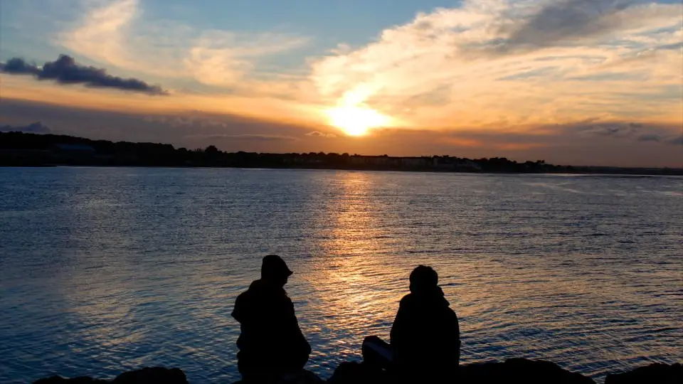Sexdate Köln: zwei Menschen sitzen bei Sonnenuntergang am Wasser