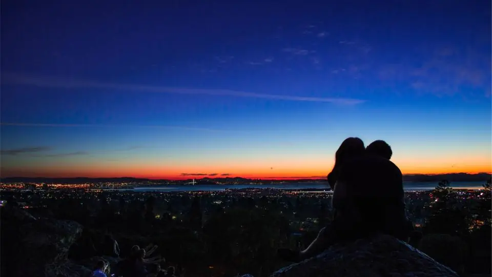 Sexdate München: ein Paar sitzt eng beieinander über einer Stadt in der Dämmerung